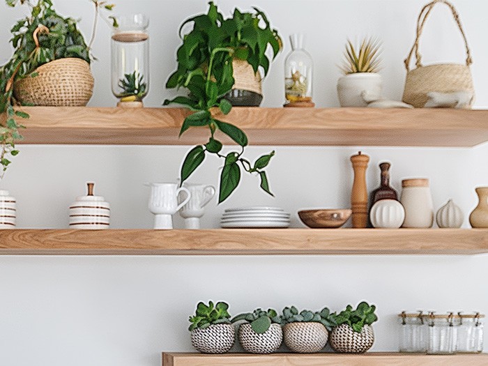 A white kitchen with open wood shelving filled with bowls, plates, and potted plants.