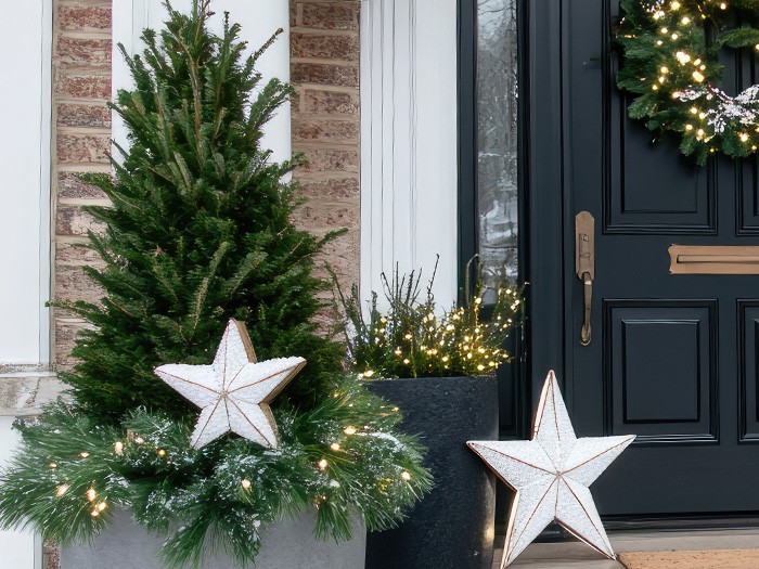 A front porch featuring miniature pine trees with ornaments.